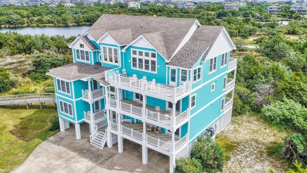 A multi-story house with a balcony, surrounded by greenery and a body of water.