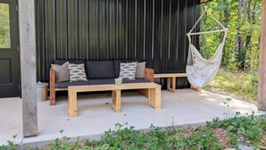 A wooden bench seating area with a hanging hammock, a black wall, and a view of greenery. - Forest Cabin w/ Stunning Wall of Windows (Jackson)