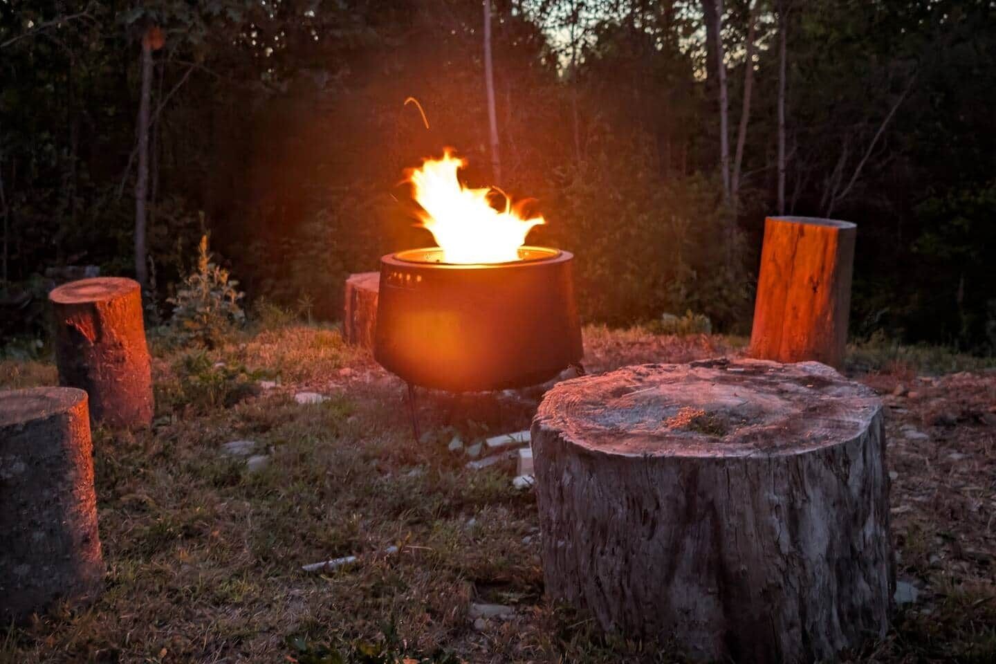 A campfire with a metal pot in a forest setting.