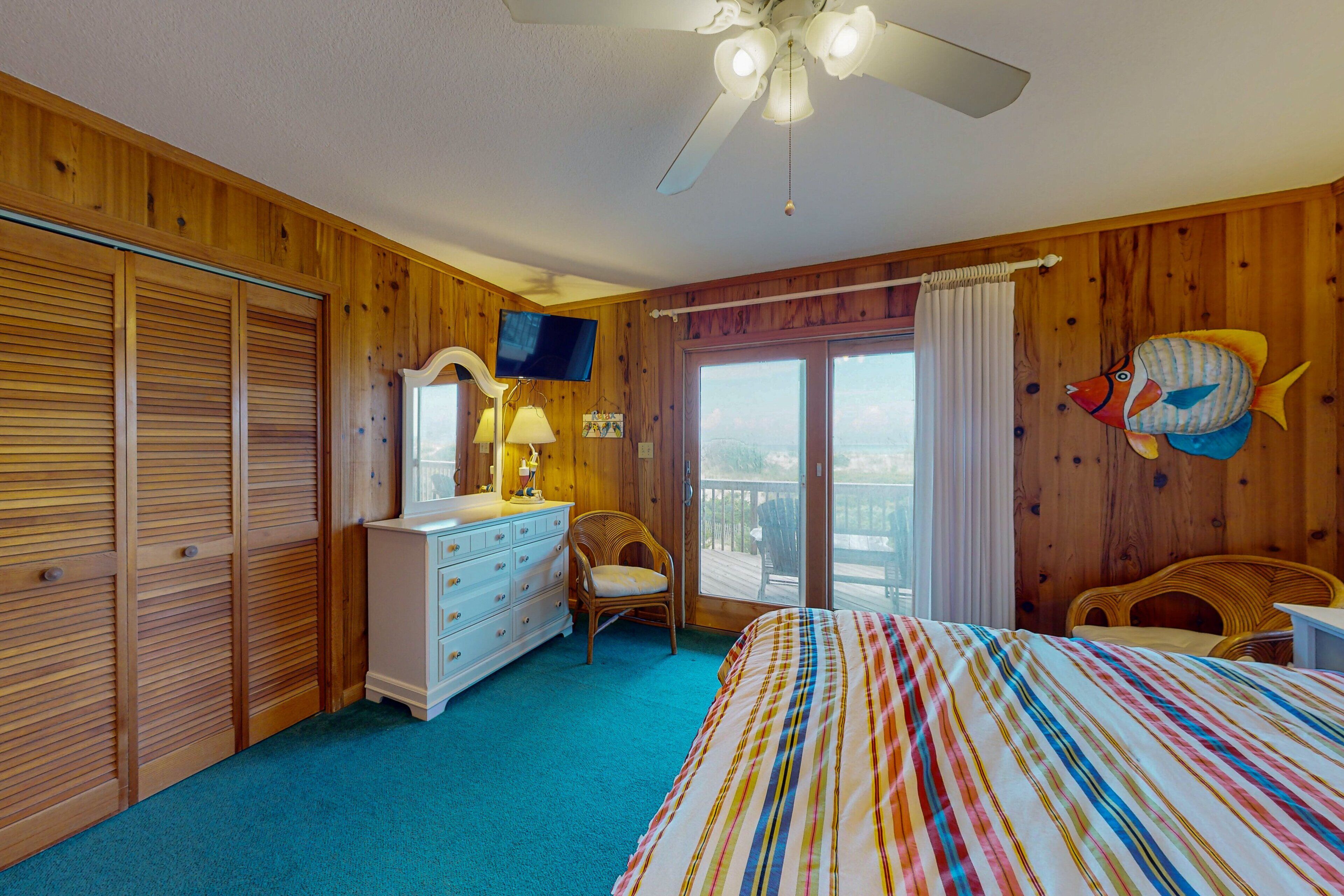 A bedroom with wooden paneling, a bed with a striped bedspread, a dresser, a chair, a television, and a window with curtains.