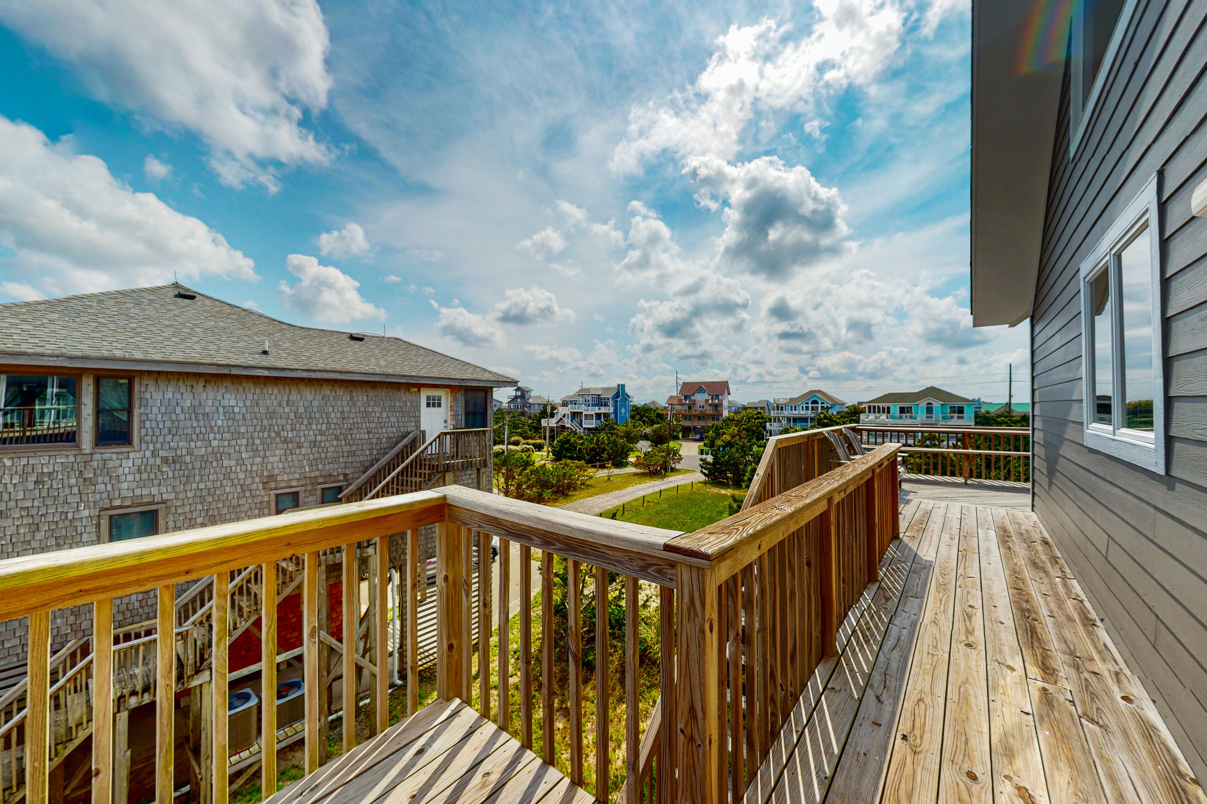 A wooden deck with a view of a residential area, including houses and a clear sky.