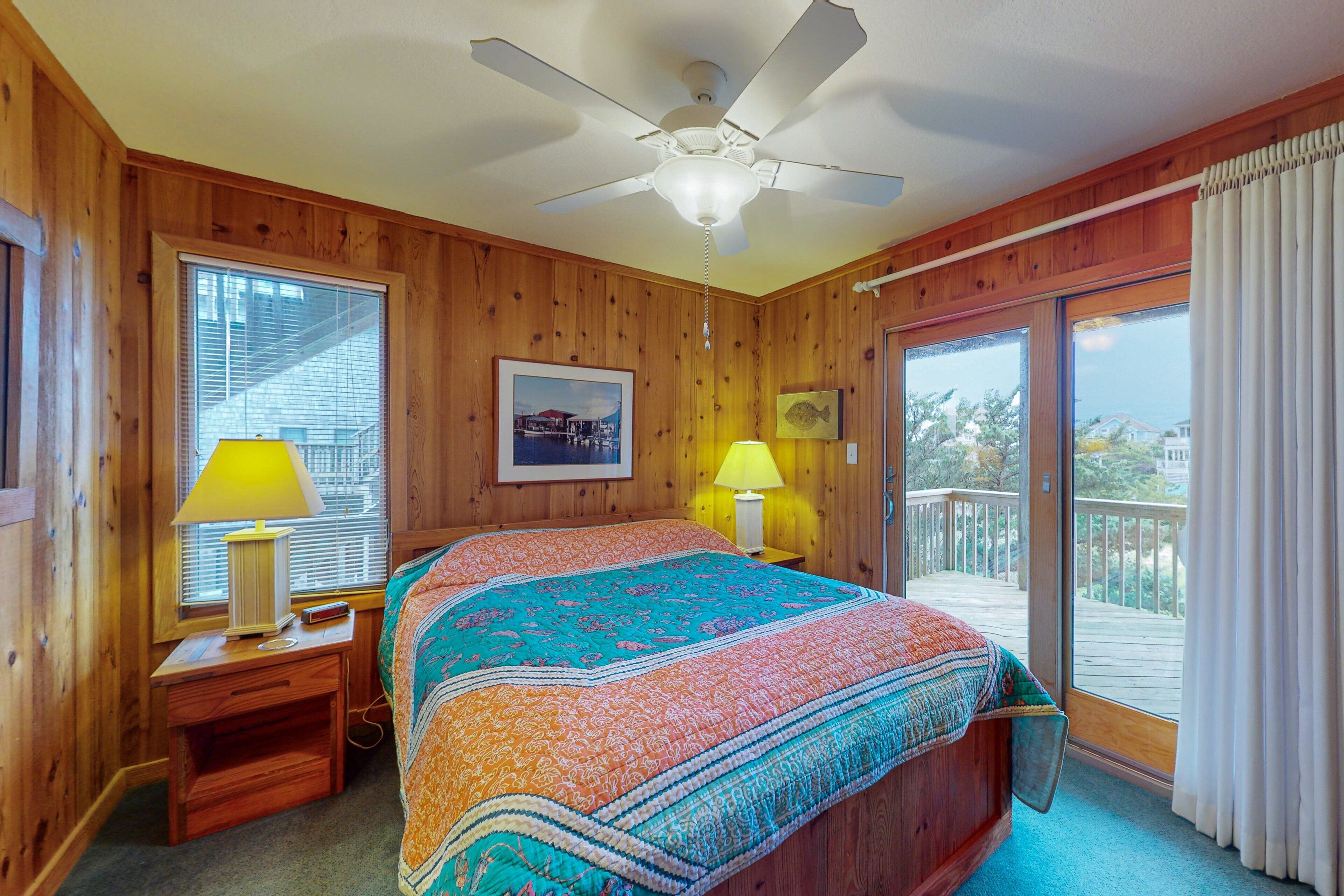 Dormitorio con paneles de madera, cama, dos lámparas de noche, ventilador de techo y balcón con vistas.