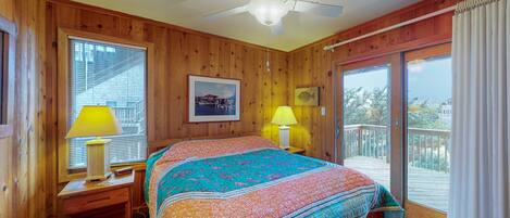Dormitorio con paneles de madera, cama, dos lámparas de noche, ventilador de techo y balcón con vistas.
