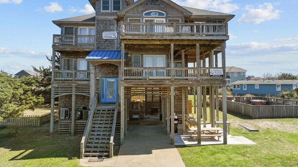 Une maison en bois à plusieurs étages, dotée d’un balcon, d’un porche et d’un escalier menant à l’entrée.