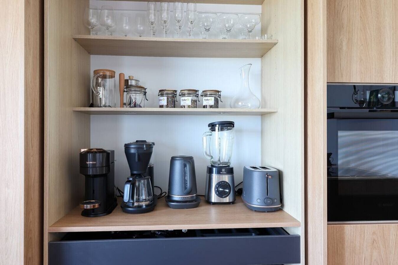 A kitchen with a coffee maker, blender, toaster, and glass jars on shelves.