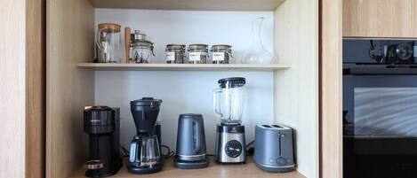 A kitchen with a coffee maker, blender, toaster, and glass jars on shelves.