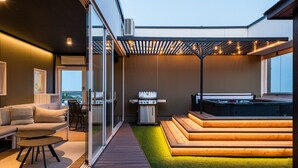 En udendørs terrasse med grill, jacuzzi og siddeområde med udsigt over byen.