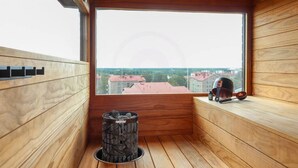 Et sauna-rum med trævægge, stort vindue, saunaovn og en sauna-børste på vindueskarmen.
