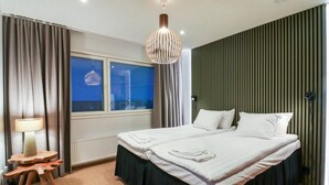 Et moderne soveværelse med en stor seng, et sengebord med lampe og et vindue med skodder.