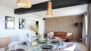 Et moderne spiseområde med et glasbord dækket til fire personer, en brun lædersofa og en høj gulvlampe.