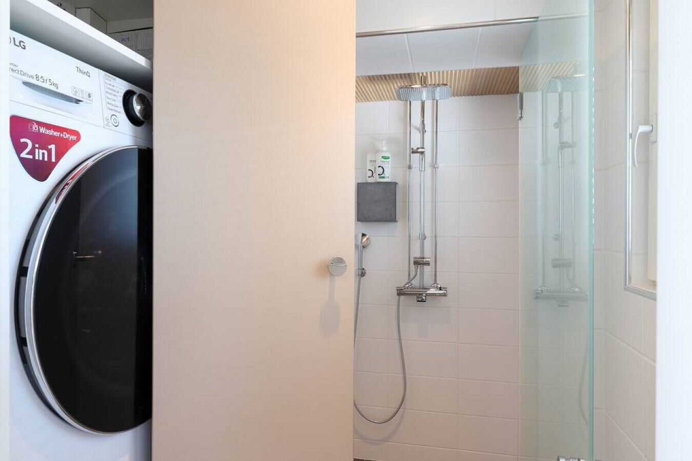 Un bagno compatto con lavatrice, cabina doccia in vetro e piccolo ripiano con articoli da toilette.
