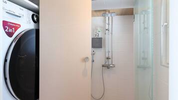 Un bagno compatto con lavatrice, cabina doccia in vetro e piccolo ripiano con articoli da toilette.