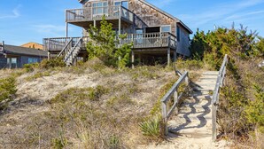 A two-story beachfront house with a wooden deck and stairs leading to a balcony. - Yankee Clipper 204: Oceanfront, balcony, ocean views (Avon)