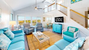 A spacious living room with a high ceiling, large windows, and a staircase leading to an upper level. - Yankee Clipper 204: Oceanfront, balcony, ocean views (Avon)