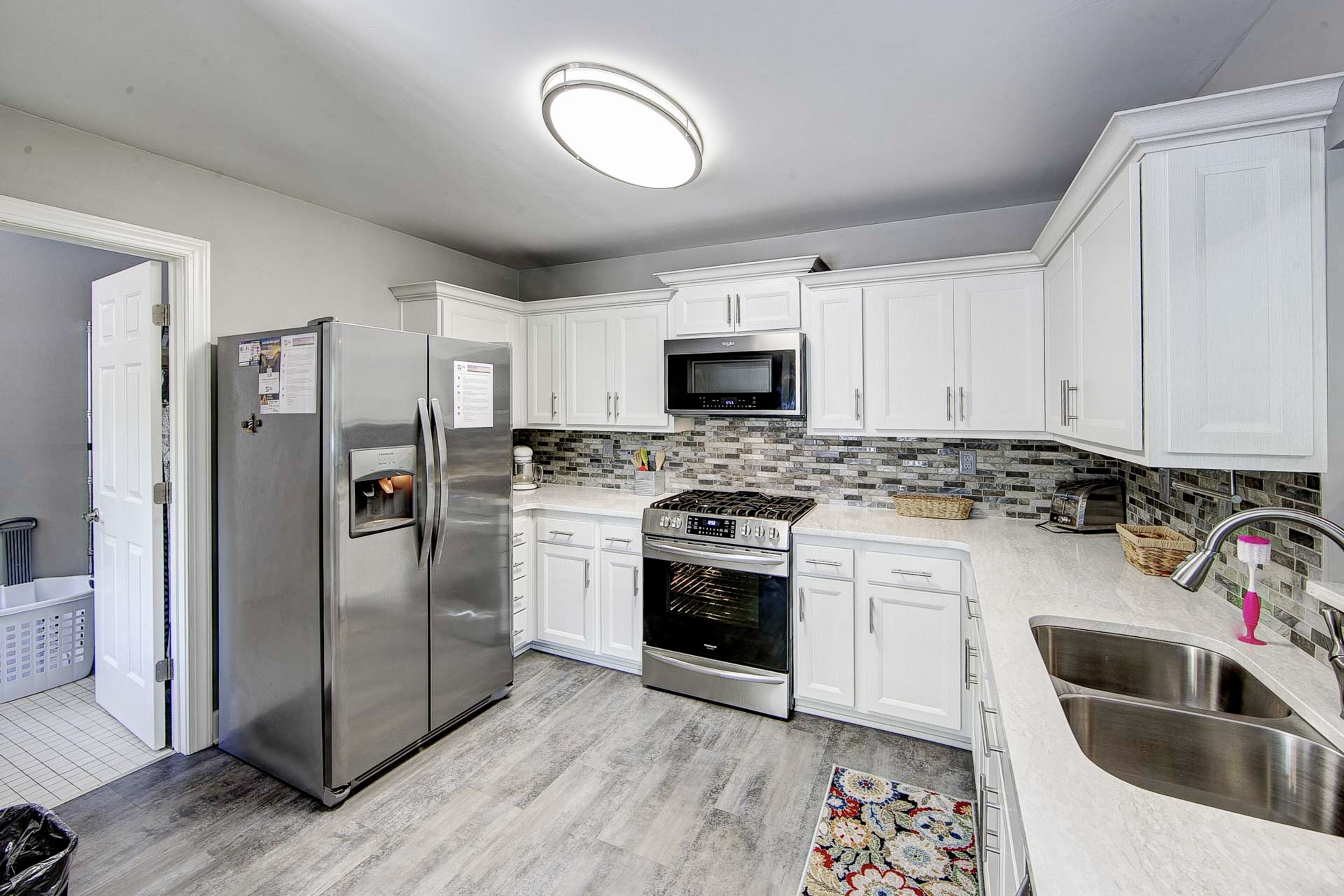 A modern kitchen with white cabinets, stainless steel appliances, a microwave, oven, and a sink.