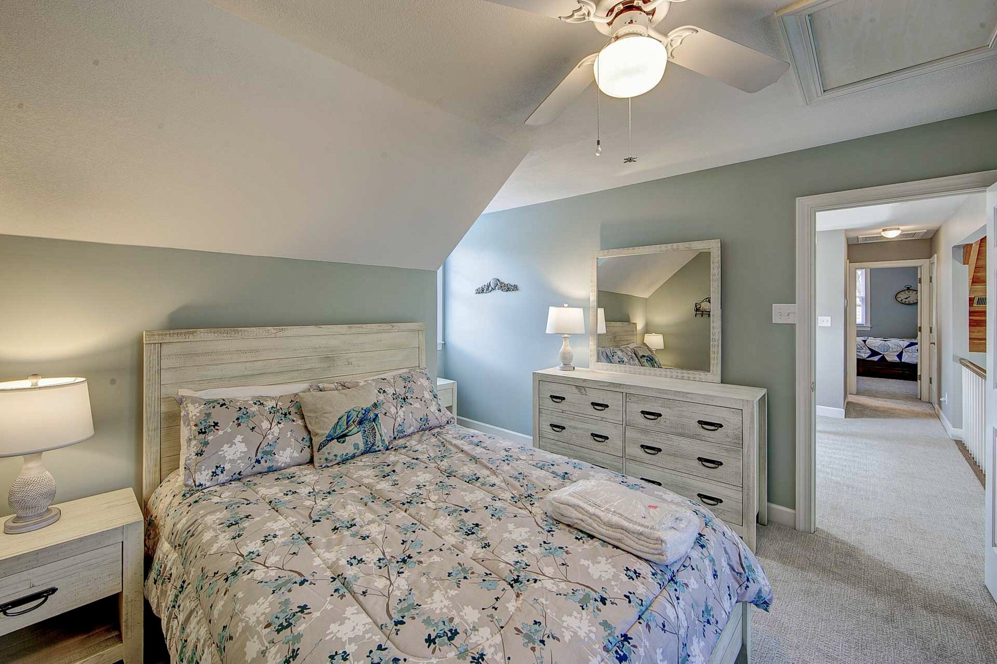 Un dormitorio con cama, mesitas de noche, cómoda, ventilador de techo y espejo.