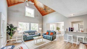 A spacious living area with a high ceiling and wooden beams, a kitchen with white bar stools, and a dining area with a table and chairs. - Charming 3BR home in Frisco with Wifi, Full Kitchen and Private Hot Tub (Frisco)