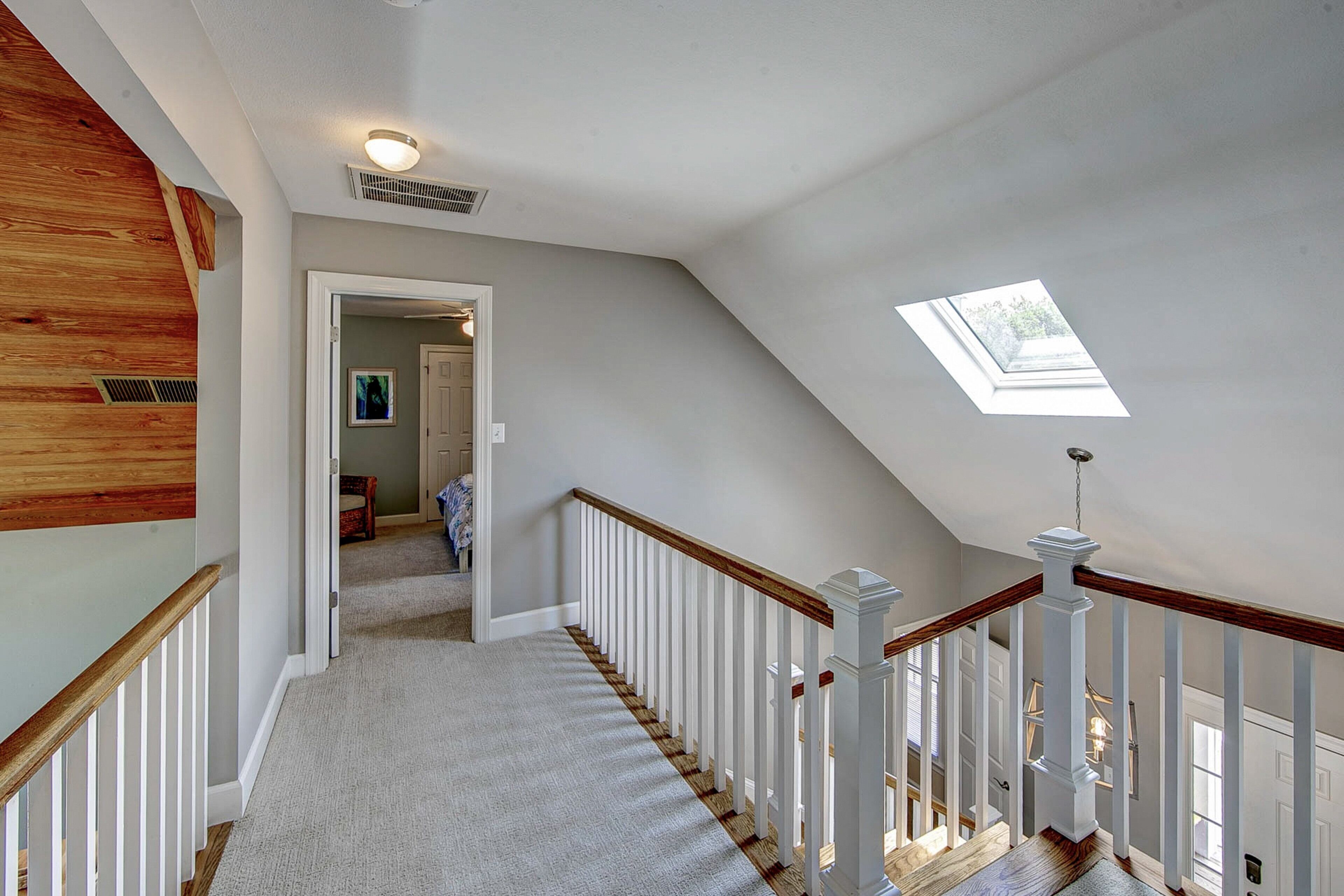 Un escalier avec des rampes blanches et des marches en bois menant à une mezzanine dotée d’un puits de lumière.