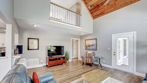 A spacious living room with a high ceiling, a wooden staircase, a television, a sofa, and a dining table. - Charming 3BR home in Frisco with Wifi, Full Kitchen and Private Hot Tub (Frisco)