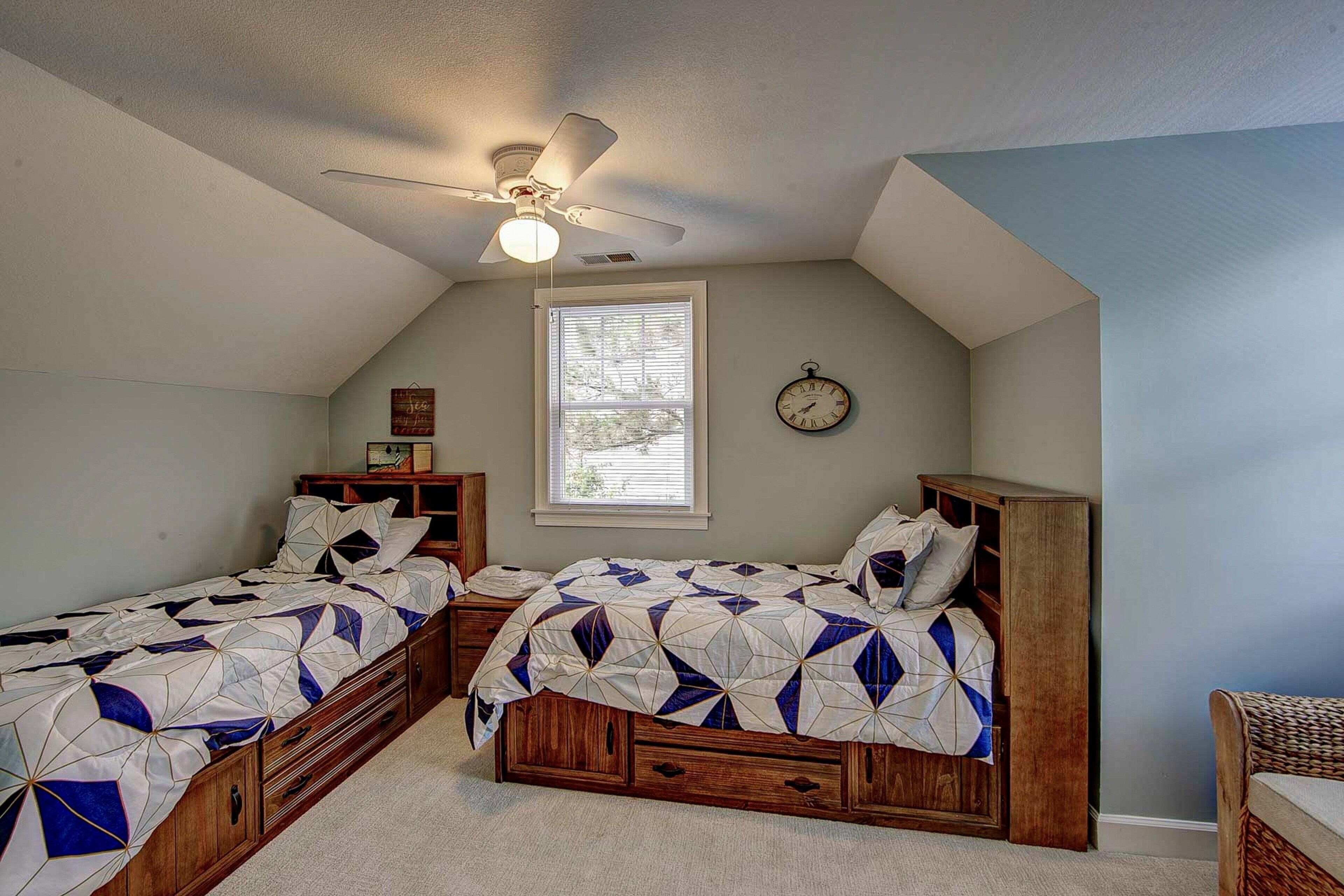 A bedroom with two single beds, a ceiling fan, a clock, and a window with blinds.