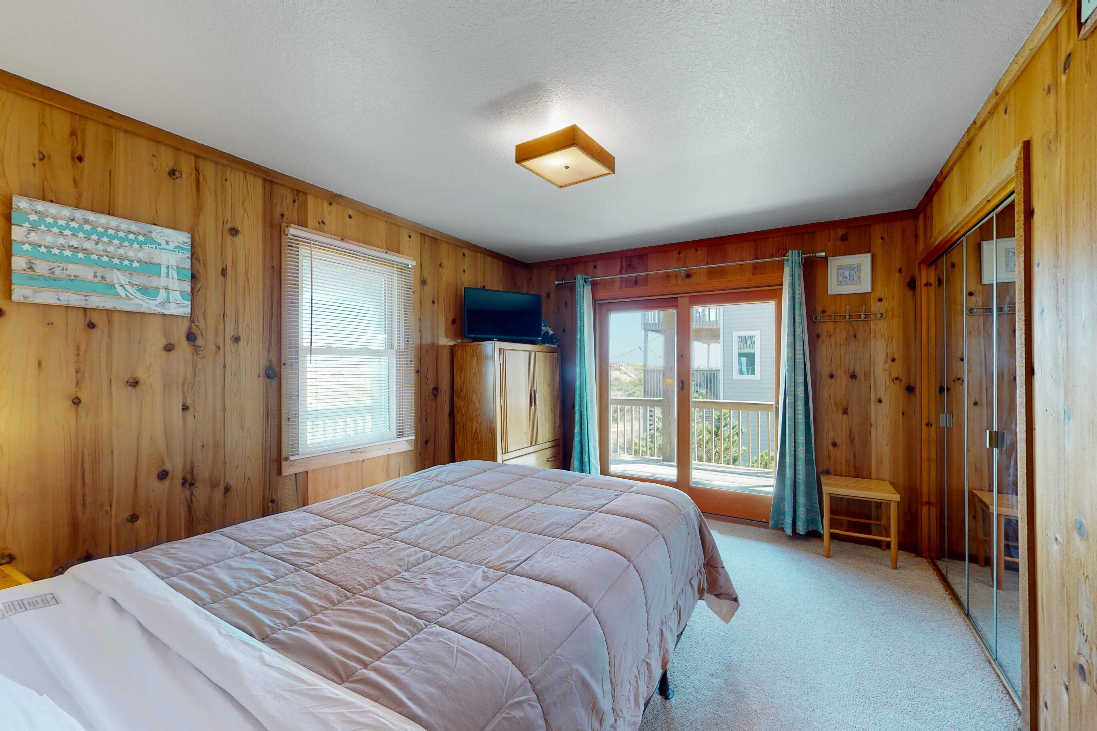 Ein Schlafzimmer mit Holzwänden, einem Bett, einem Fernseher, einem Fenster und einer Balkontür.