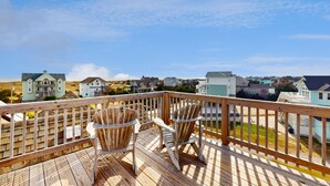 Een houten terras met twee Adirondack-stoelen met uitzicht op een woonwijk met huizen.