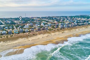 An aerial view of a coastal residential area with houses along the beach, a clear sky, and the ocean in the foreground. - 6 BR house Dog friendly with mini golf, pool/hot tub, & game room (Waves)