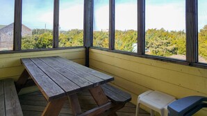 Une terrasse en bois avec une table de pique-nique et un petit tabouret, donnant sur une zone boisée.