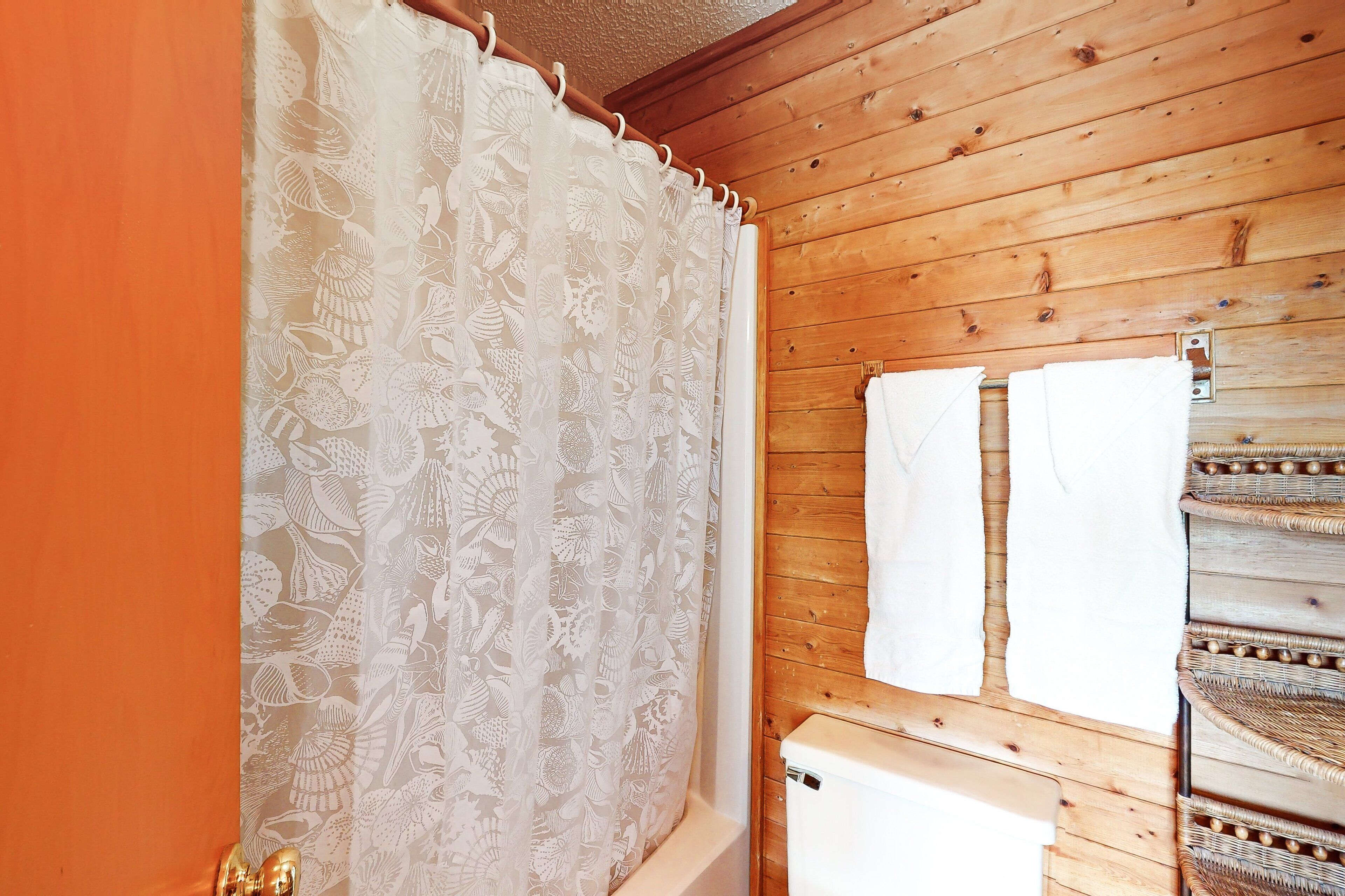 A bathroom with a wooden ceiling, a shower curtain with a floral pattern, and a towel rack with two white towels.