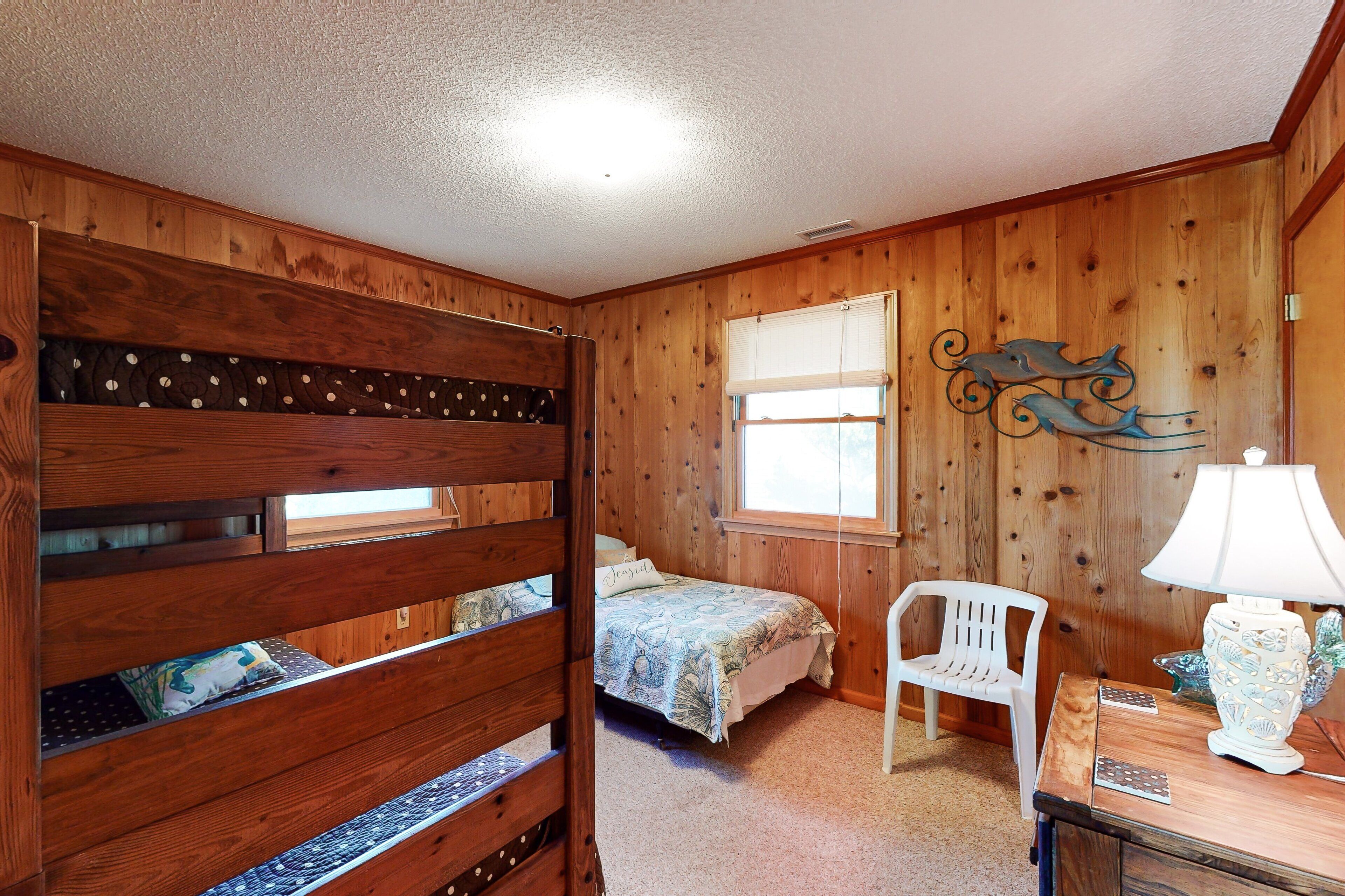 Quarto com cama beliche, uma cama de solteiro, janela, cadeira e abajur.