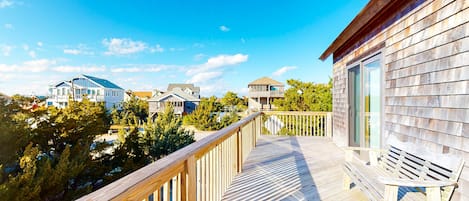 A wooden deck with a bench, overlooking a residential area with houses and trees.