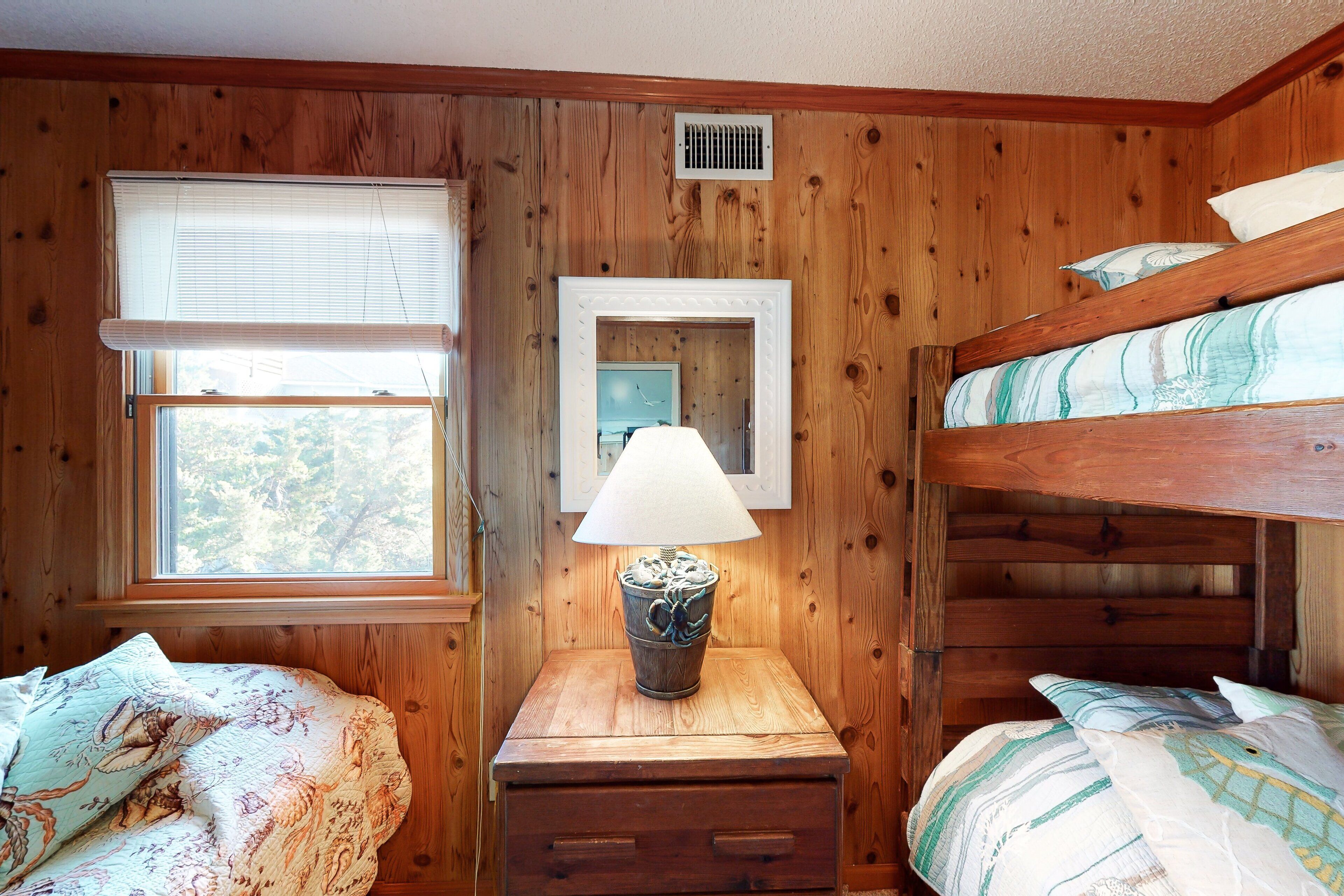 Une pièce en bois avec des lits superposés, une fenêtre avec des stores, une lampe sur une table en bois et un miroir au mur.