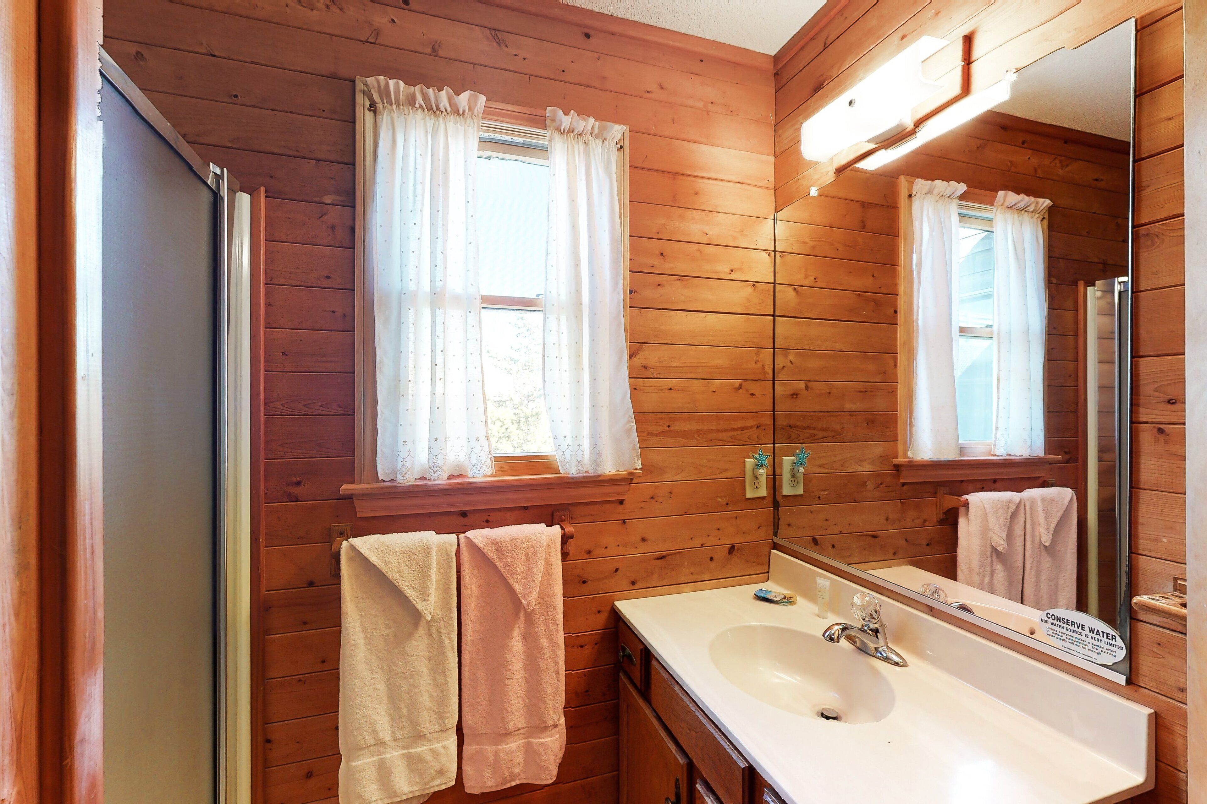 A wooden cabin bathroom with a sink, mirror, and two towels.