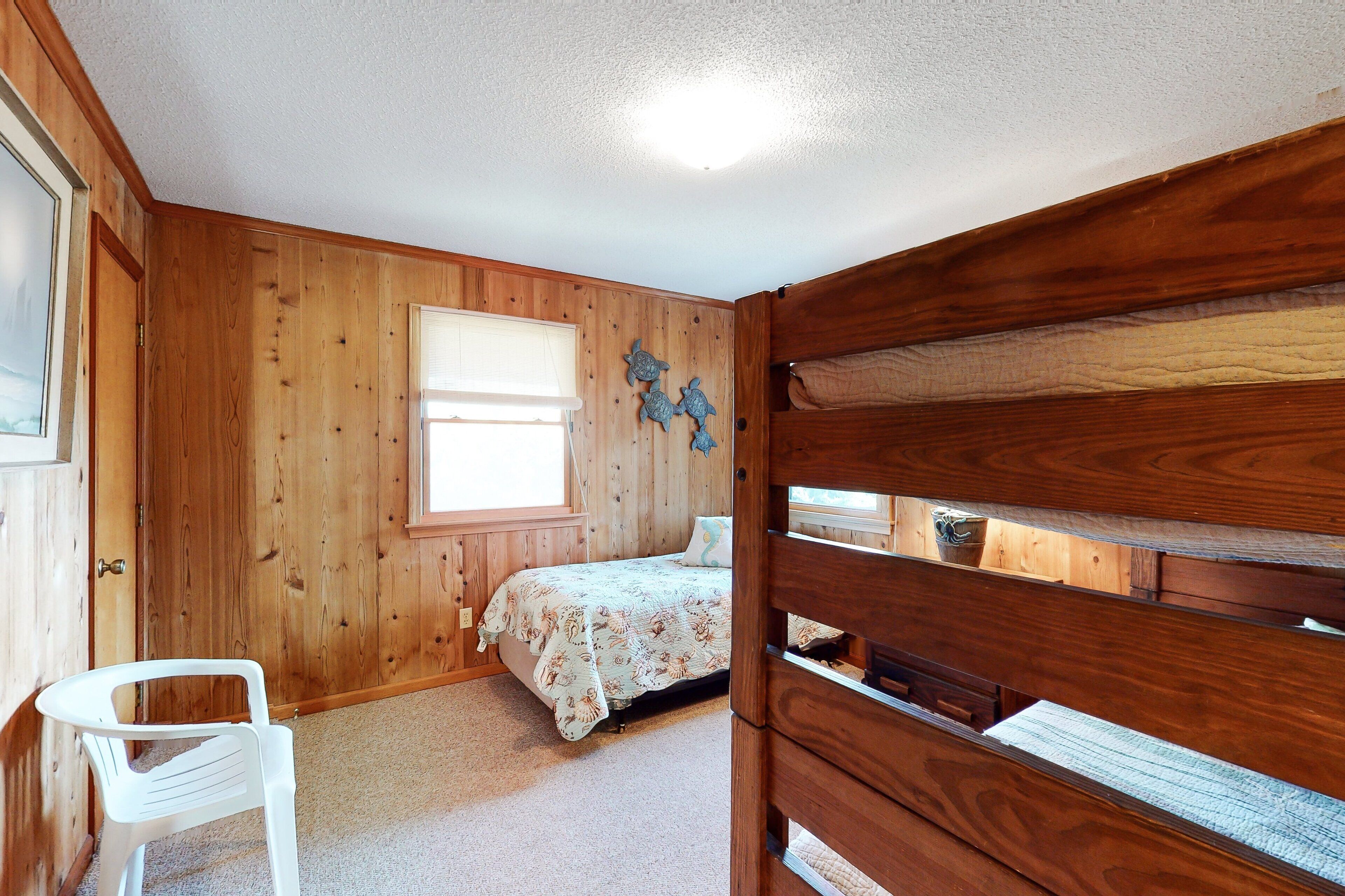 Una camera da letto con pareti in legno, un letto con copripiumino floreale, una finestra e una sedia bianca.