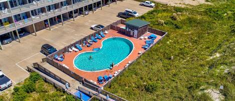 An aerial view of a hotel with a swimming pool surrounded by lounge chairs and a deck.