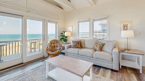 A living room with a sofa, a coffee table, a chair, and a lamp. There are two windows with a view of the ocean. - Fun beachfront home w/shared pool, WiFi, private washer & dryer, central AC (Avon)