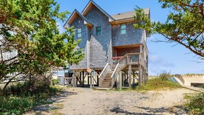 A two-story wooden building with a porch and stairs leading to the entrance. - Fun beachfront home w/shared pool, WiFi, private washer & dryer, central AC (Avon)