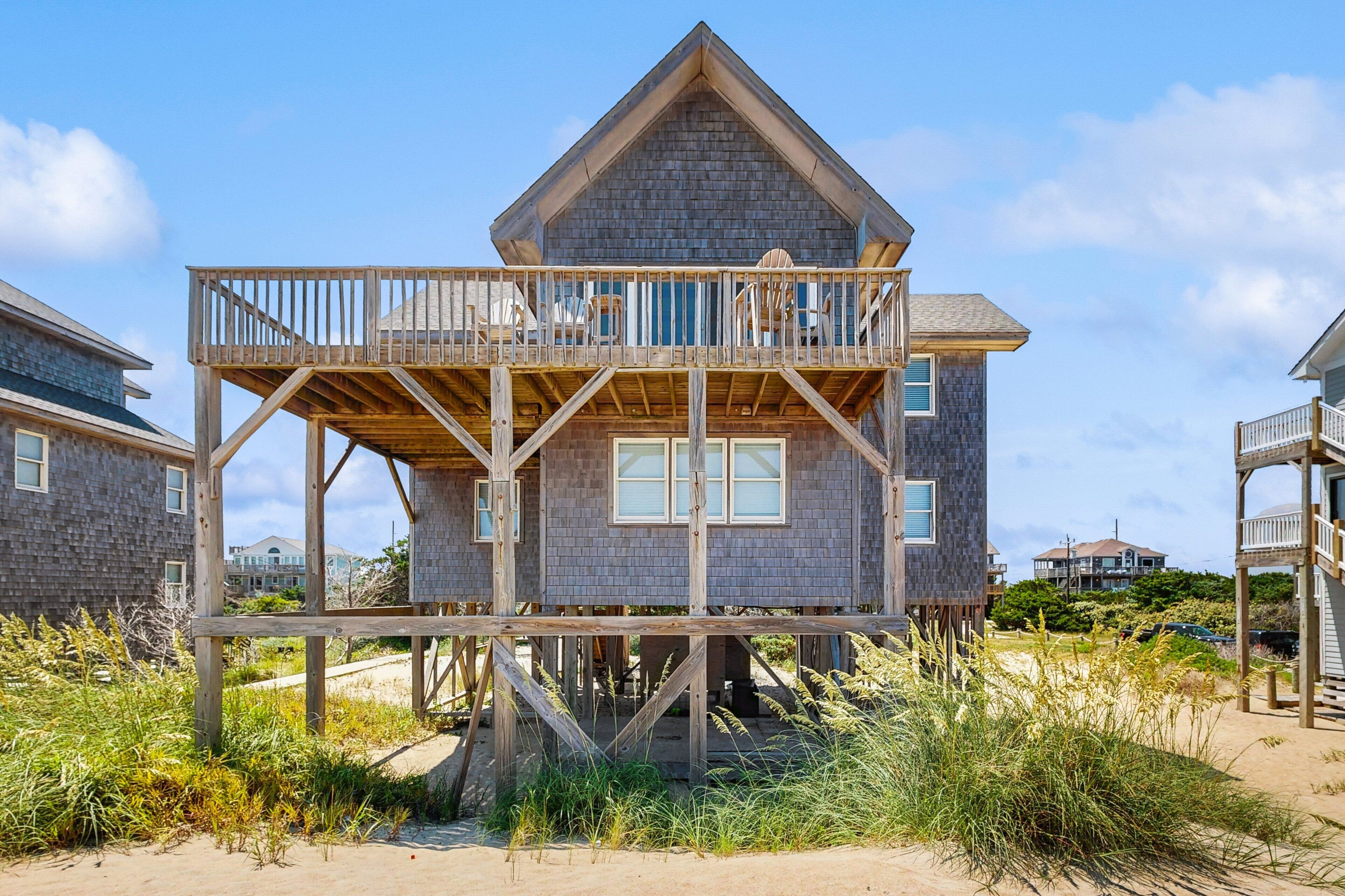 A wooden house with a balcony on stilts, surrounded by beach vegetation.