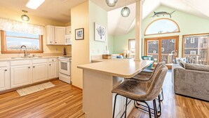 A kitchen with a bar area, wooden flooring, and a view of the outside. - Semi-Ocean Front Retreat with Full Kitchen, Wifi, Outdoor Shower and A/C (Avon)