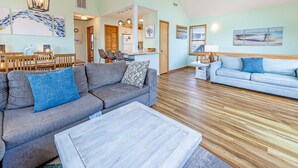 A spacious living room with a grey sofa, a coffee table, and a dining area with a wooden table and chairs. - Semi-Ocean Front Retreat with Full Kitchen, Wifi, Outdoor Shower and A/C (Avon)