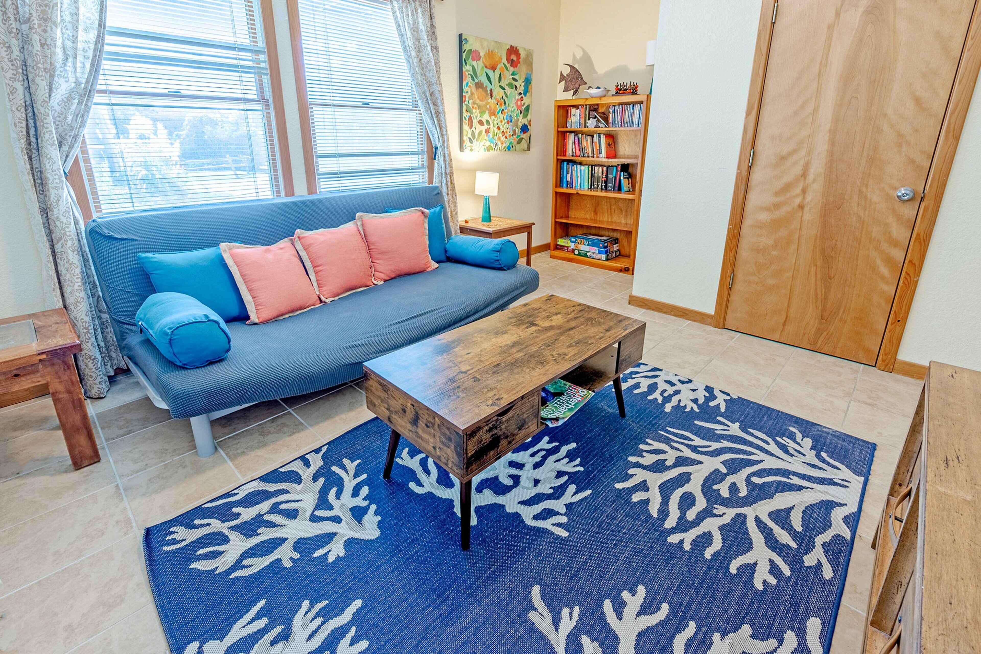 A living room with a blue sofa, wooden coffee table, and a blue rug with white coral patterns.