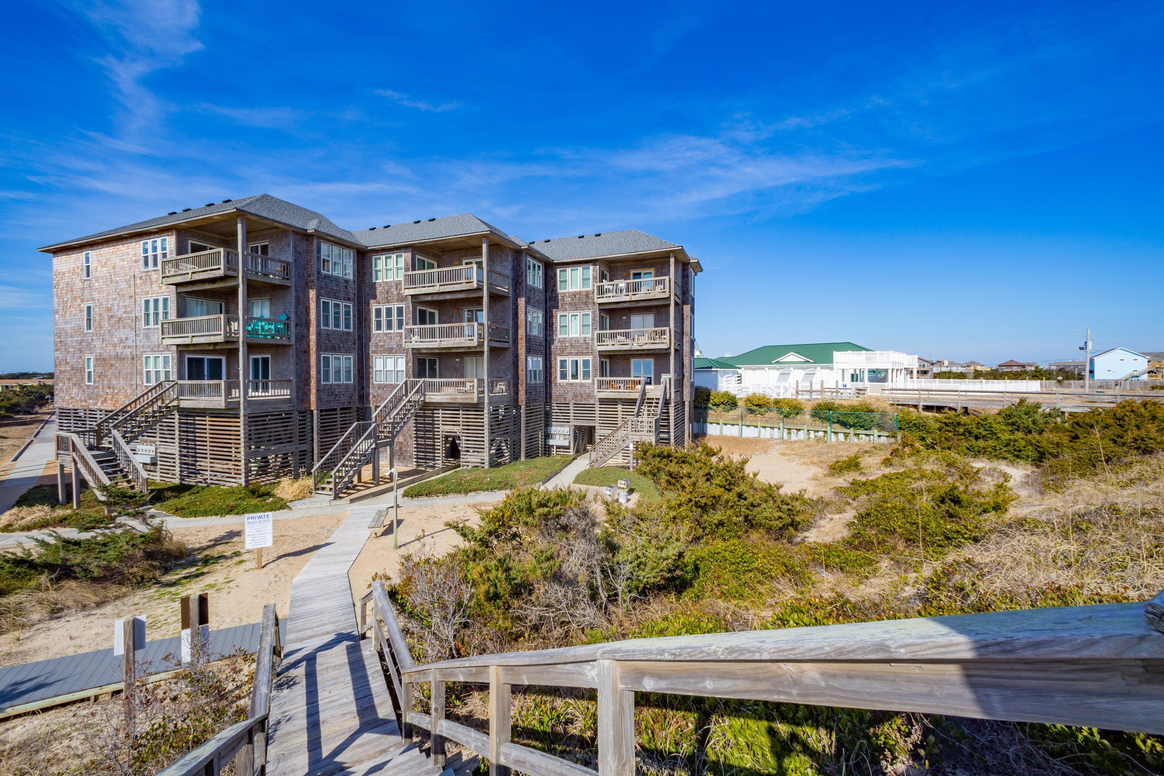 A multi-story building with balconies, a wooden deck, and a beach view.