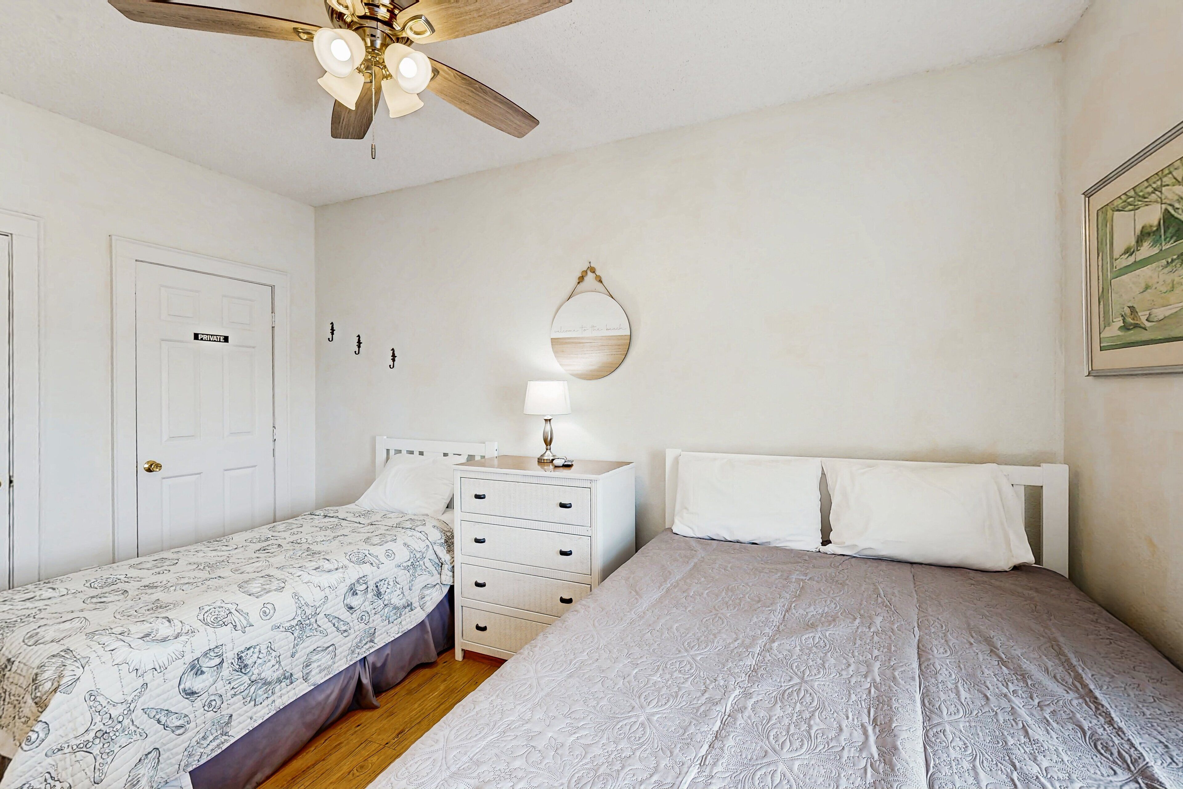 A bedroom with a bed, a nightstand, a dresser, a ceiling fan, and a wall-mounted mirror.