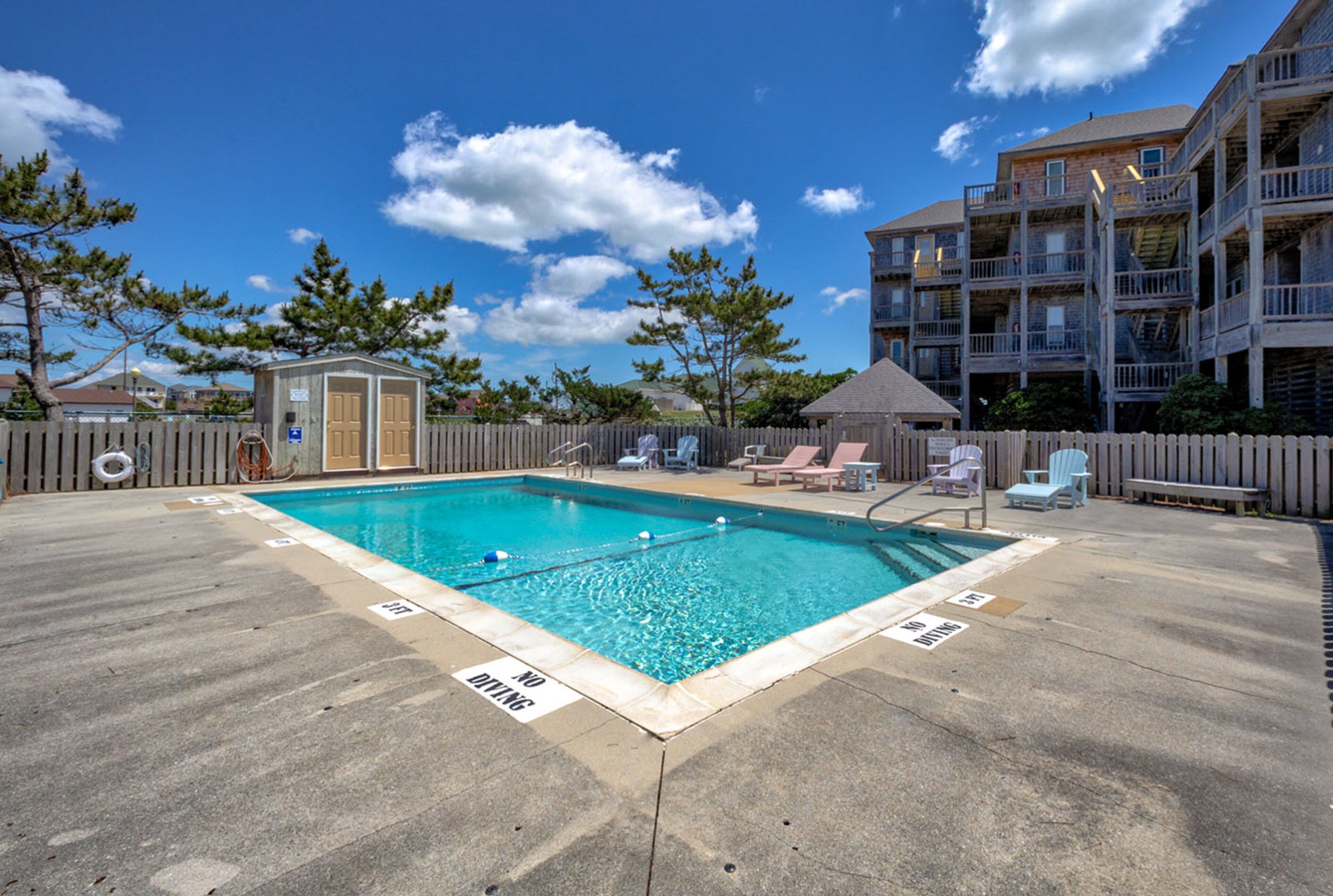 A rectangular swimming pool with a wooden deck surrounding it, a small wooden structure, and a wooden fence.
