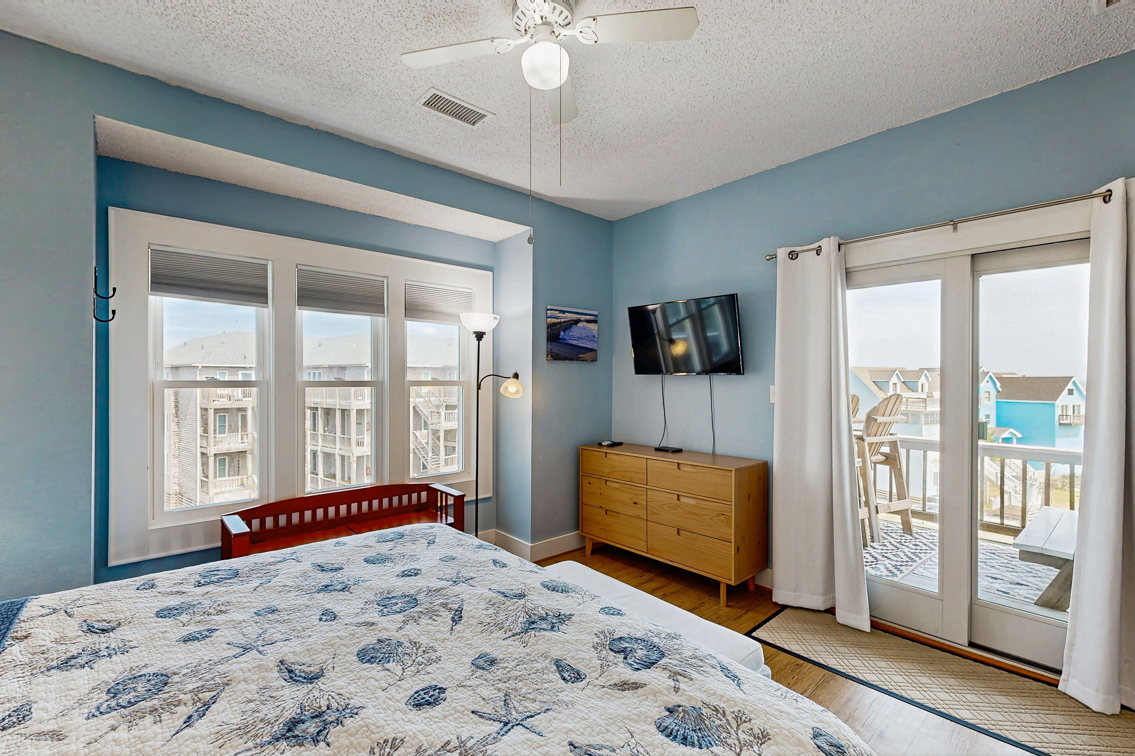 A bedroom with a bed, a dresser, a TV, and a balcony with a view of buildings.