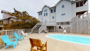 A pool area with a wooden deck, blue and white Adirondack chairs, and a wooden chair. - Oceanfront home with central AC, ocean view, private hot tub, & pool (Avon)
