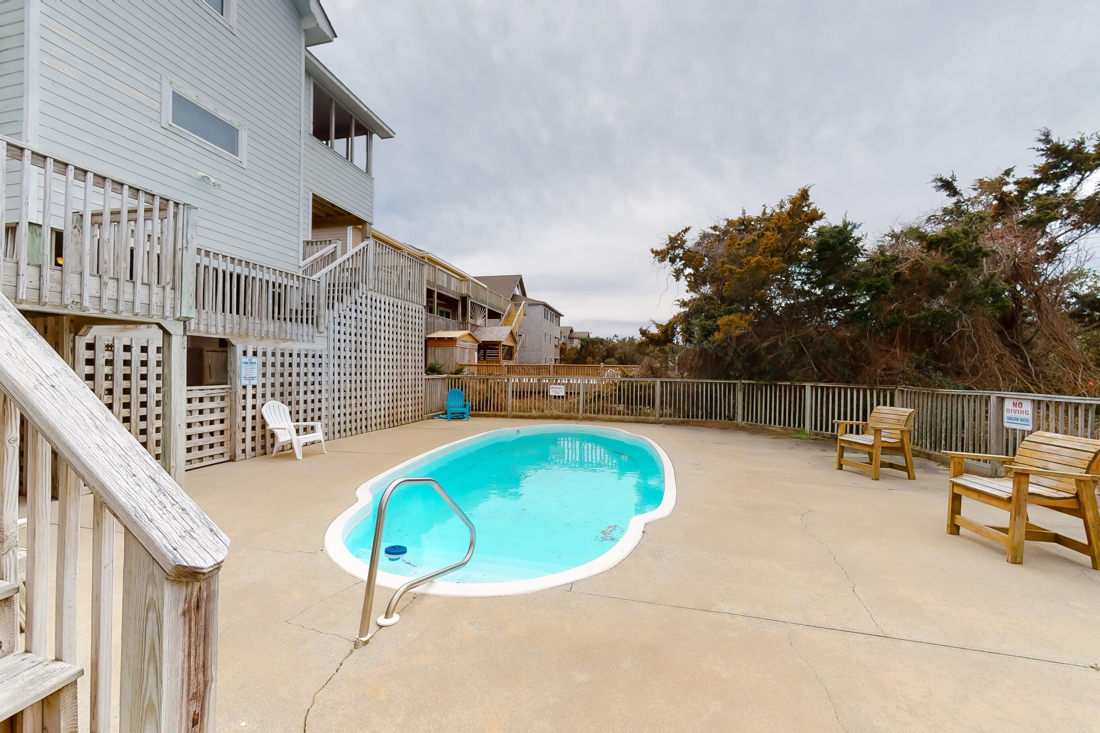 A swimming pool with a wooden deck and a fence, surrounded by a building with a balcony and a staircase.