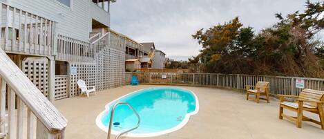 A swimming pool with a wooden deck and a fence, surrounded by a building with a balcony and a staircase.