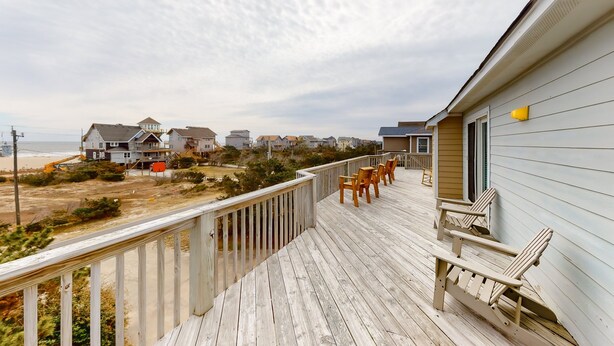 A wooden deck with chairs, overlooking a beach and houses. - Oceanfront home with central AC, ocean view, private hot tub, & pool (Avon)