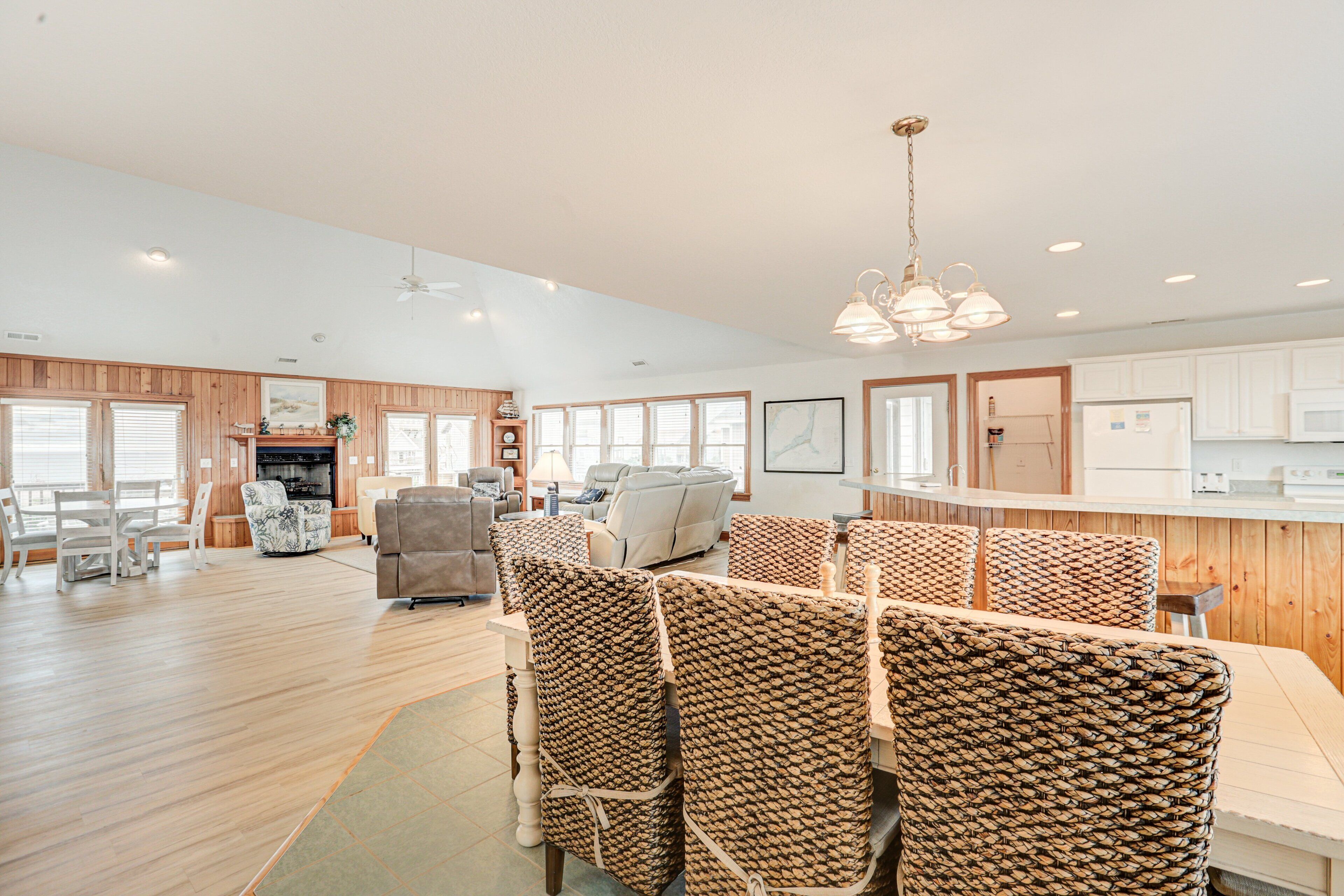 A spacious living area with a dining table, wicker chairs, a sofa, and a kitchen in the background.
